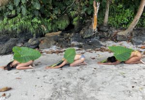 3 Women laying as "seeds" on the beach in "Petite Tacaribe" the north coast of Trinidad. We are hunched on the sand with a giant forest leaf covering our bodies. 