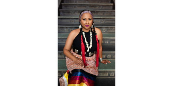 A photo of Sequoyah Hunter-Cuyjet leaning on steps in a colorful dress with a white necklace.