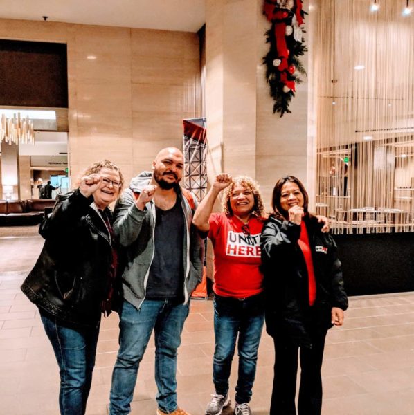 Maintainers Fellow Maximillian Alvarez stands with hotel workers in an ample lobby with Christmas decorations with raised fist symbolizing solidarity.