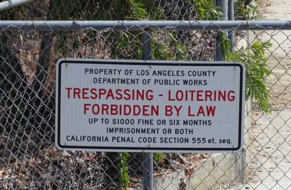 A sign on a fence reading "Trespassing - Loitering Forbidden by Law".