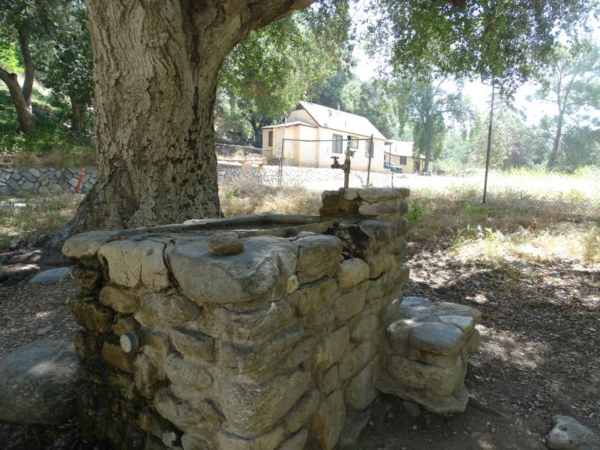 A drinking fountain with a house in the background behind a fence.