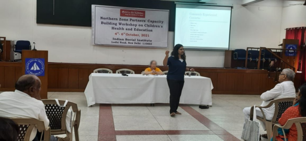 Himani Kulkarni conducting a workshop in a large room while participants sit facing her. There is a projector screen behind her explaining commonly experienced mental health concerns.)
