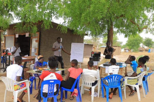Mathew facilitating a training on repair of electronics to a group of young refugee Women under a tree at the Bright Makerspace in Eden Village