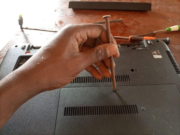  A hand holding a nail to open a laptop that is being repaired.