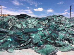 hundreds of car windshields, all partially shattered, are layered atop one another in a massive heap.