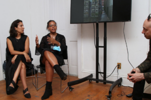 Two women sit next to a monitor and present their research