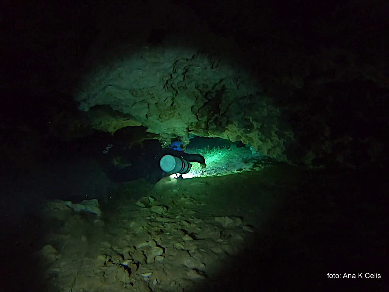 scuba diver traversing a narrow passage inside a dark cave