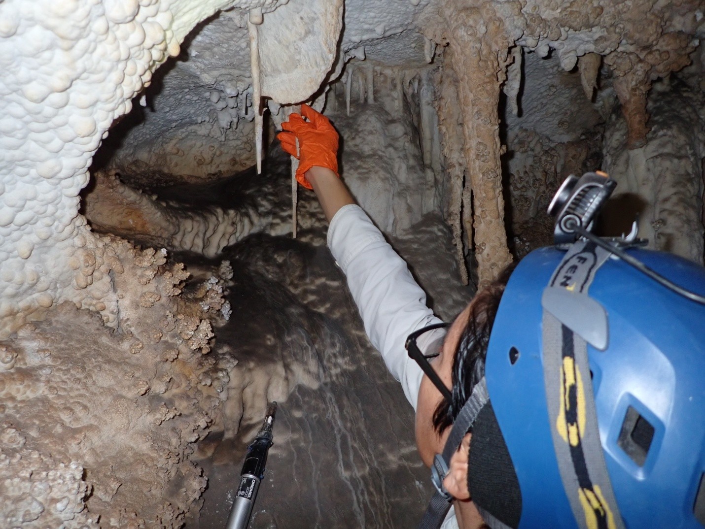 A person holds a piece of a broken speleothem reaching its possible match in the ceiling of a cave.