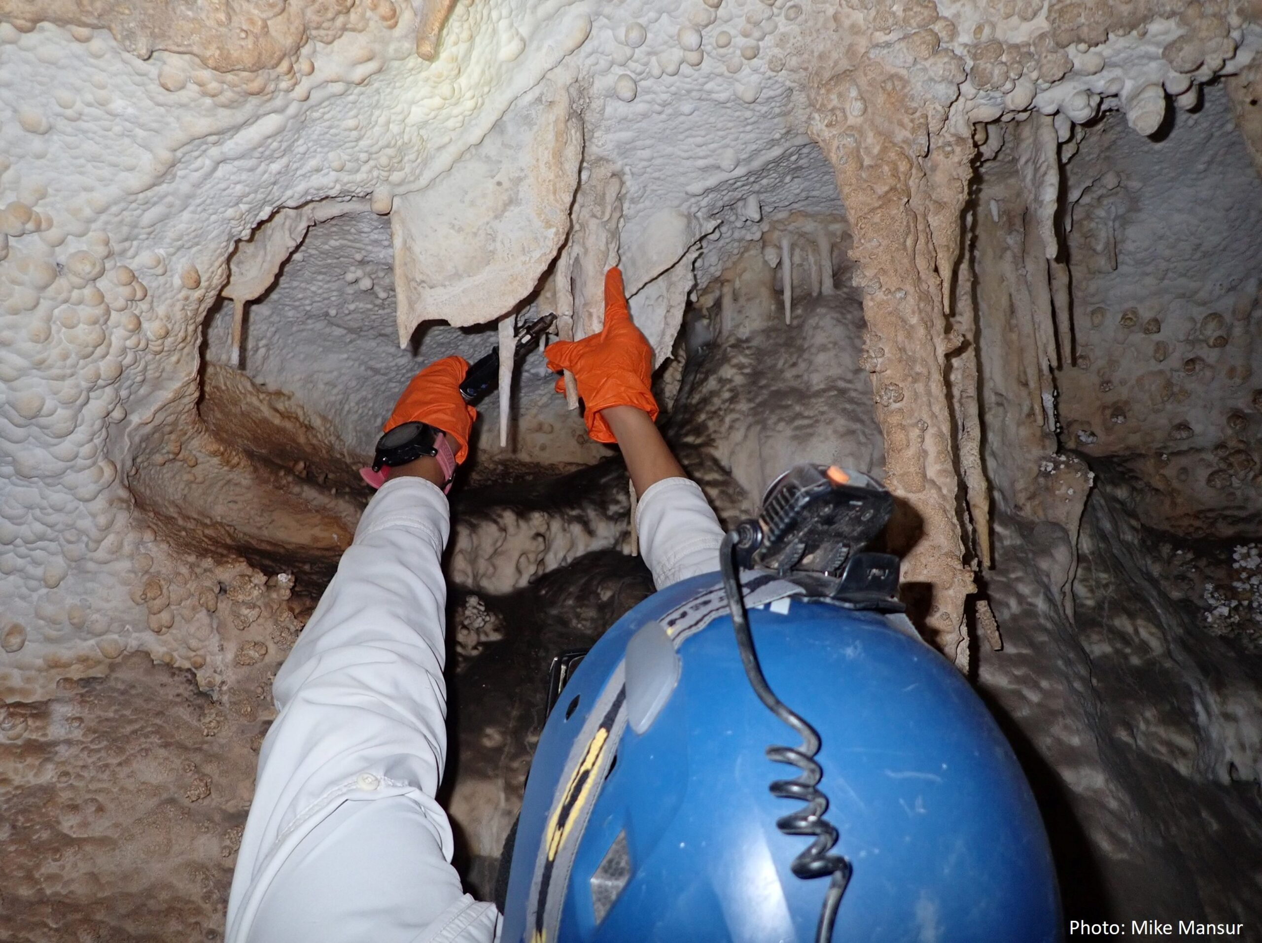 a person reaches the ceiling of a cave holding two just bonded pieces of a broken speleothem together while applying heat to the point of joint.